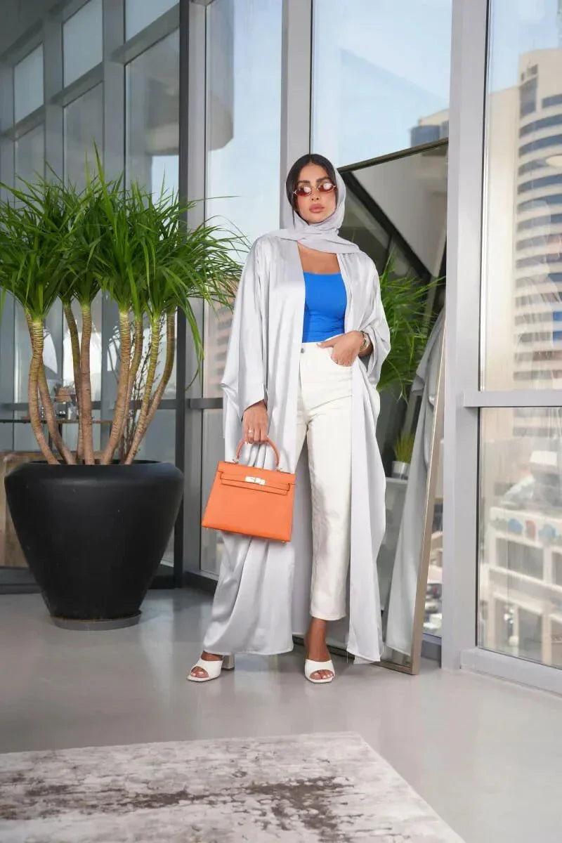 woman wearing luxurious silver silk bisht with elegant shimmer and airy fit holding orange handbag