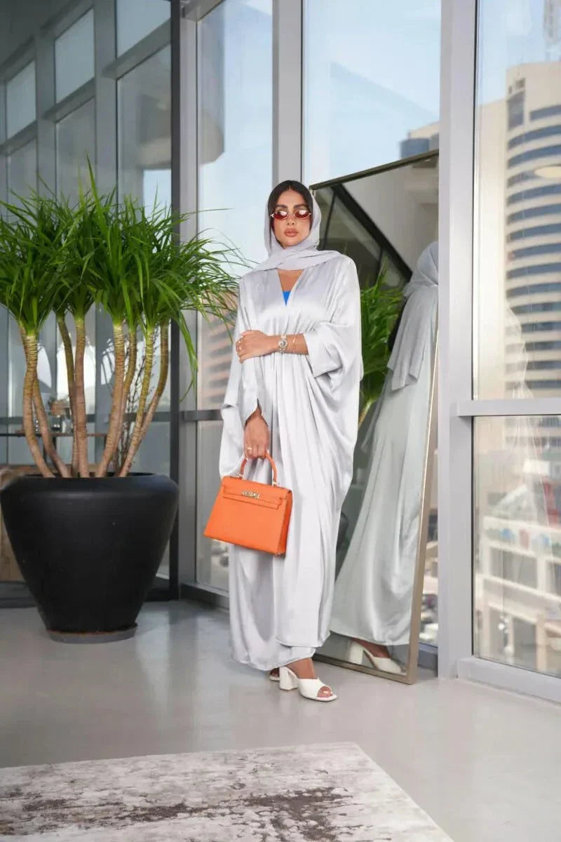 woman wearing luxurious silver silk bisht with elegant shimmer and airy fit holding orange handbag