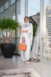 woman wearing luxurious silver silk bisht with elegant shimmer and airy fit holding orange handbag