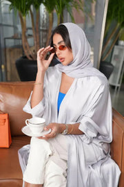 woman wearing luxurious silver silk bisht with elegant shimmer and airy fit holding orange handbag