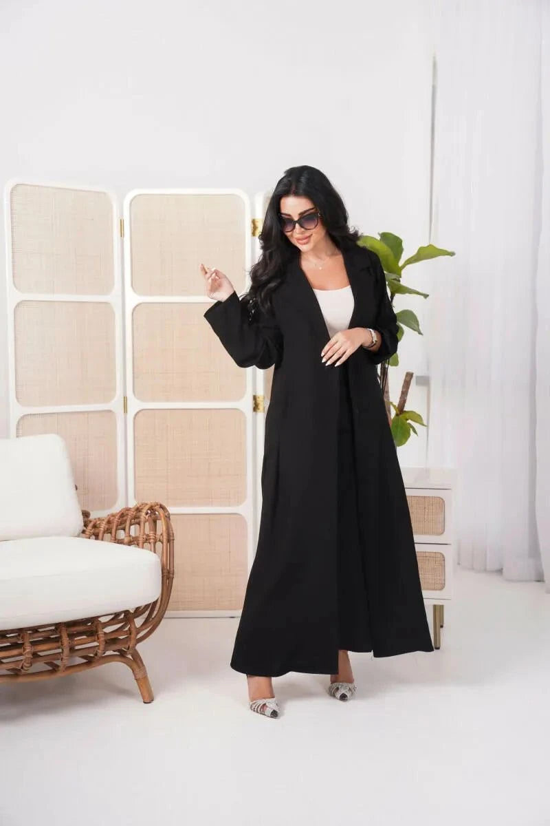 Woman wearing a classic black blazer abaya with wide sleeves and structured lapels in a modern indoor setting