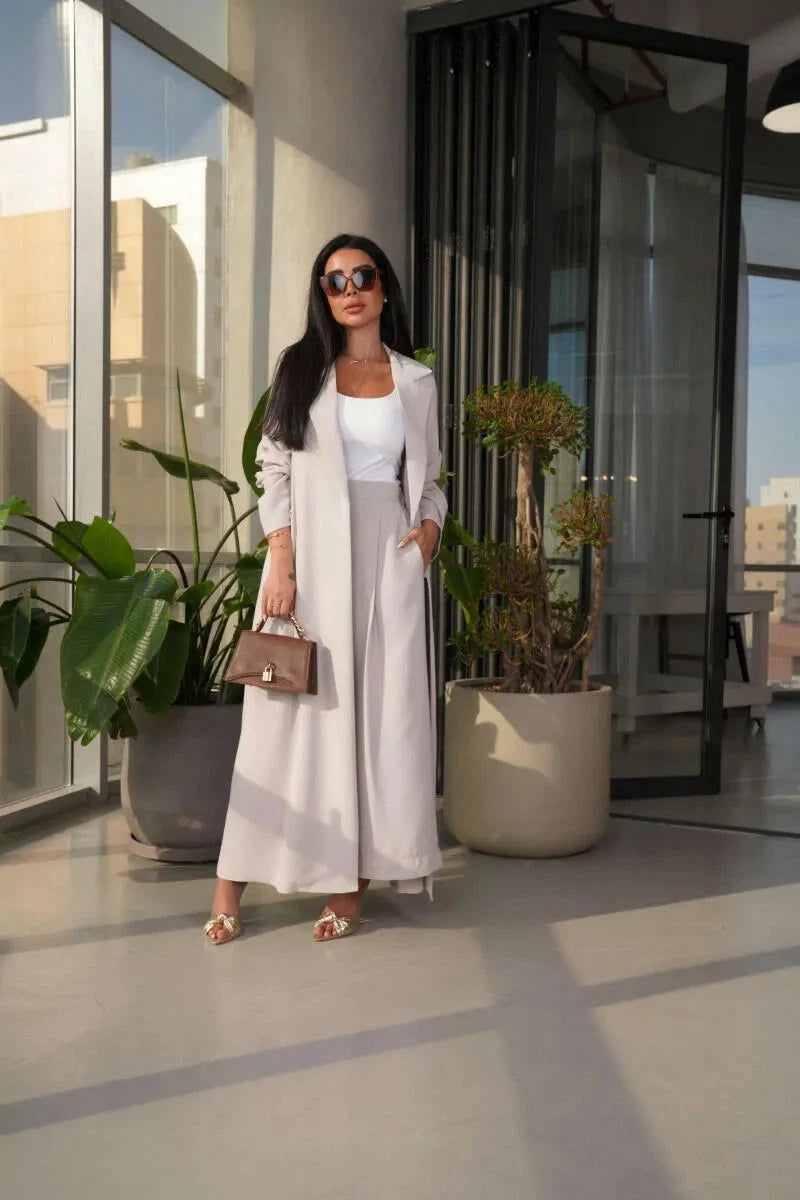 Woman wearing off-white Pearly blazer abaya with side pockets and flowy silhouette, styled with sunglasses and brown handbag indoors.