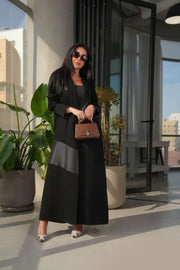 woman wearing modern black abaya with crepe and mokado fabric in a clean blazer silhouette and sharp lapels standing indoors with plants and large windows