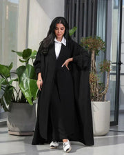 Woman wearing a free-size black blazer with wide pleated details made of soft crepe fabric.