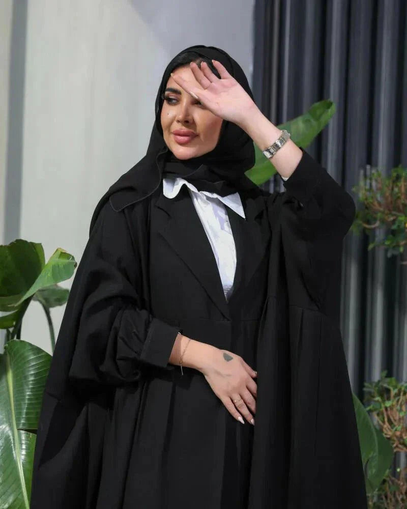 Woman wearing a free-size black blazer with wide pleated details made of soft crepe fabric.