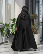 Woman wearing a free-size black blazer with wide pleated details made of soft crepe fabric.
