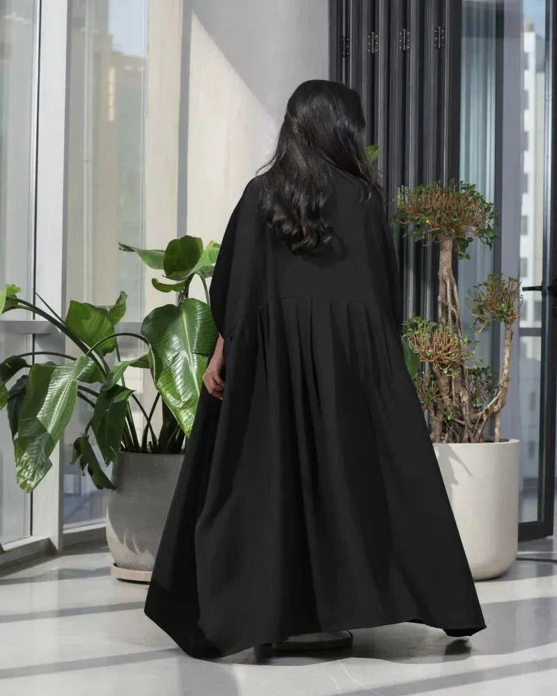 Woman wearing a free-size black blazer with wide pleated details made of soft crepe fabric.