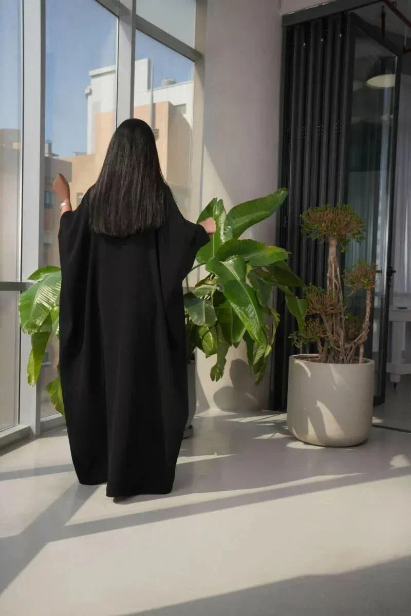 Black crepe abaya with two small leather belts worn by woman in modern indoor setting