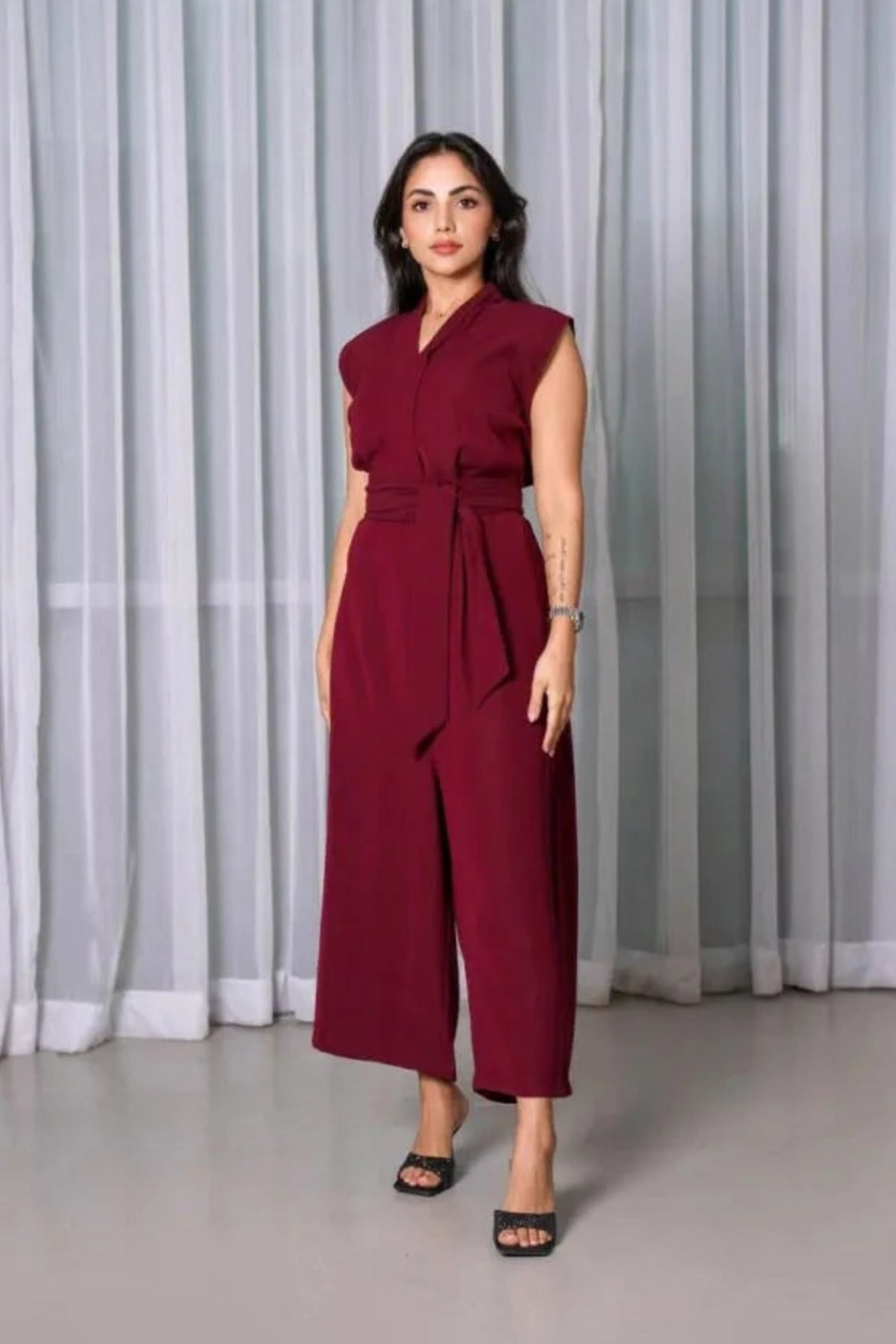 Woman wearing sleeveless burgundy crepe jumpsuit with V-neckline, wide legs, and detachable belt.