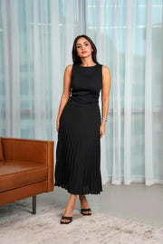 Black sleeveless pleated dress with fitted bodice and flowy skirt worn by woman indoors