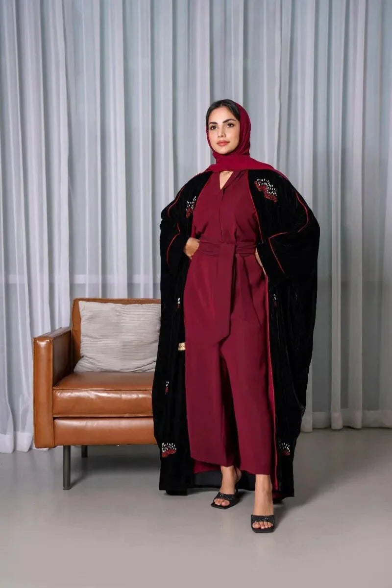 Luxurious black velvet bisht with red stone hand embroidery worn over a maroon outfit by a woman standing indoors.