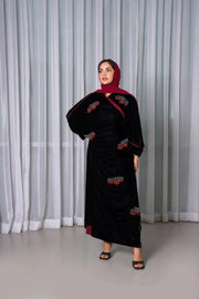 Luxurious black velvet bisht with red stone hand embroidery worn over a maroon outfit by a woman standing indoors.
