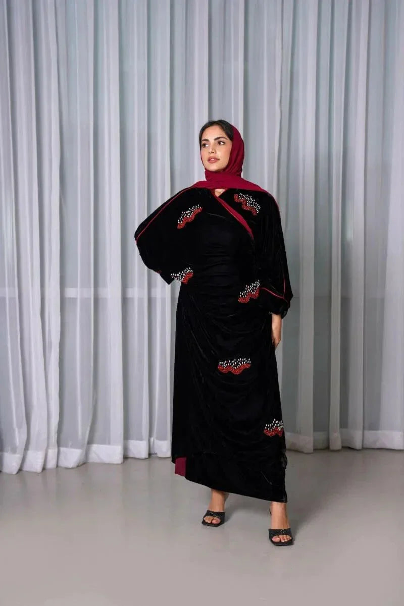 Luxurious black velvet bisht with red stone hand embroidery worn over a maroon outfit by a woman standing indoors.