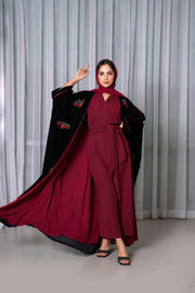 Luxurious black velvet bisht with red stone hand embroidery worn over a maroon outfit by a woman standing indoors.