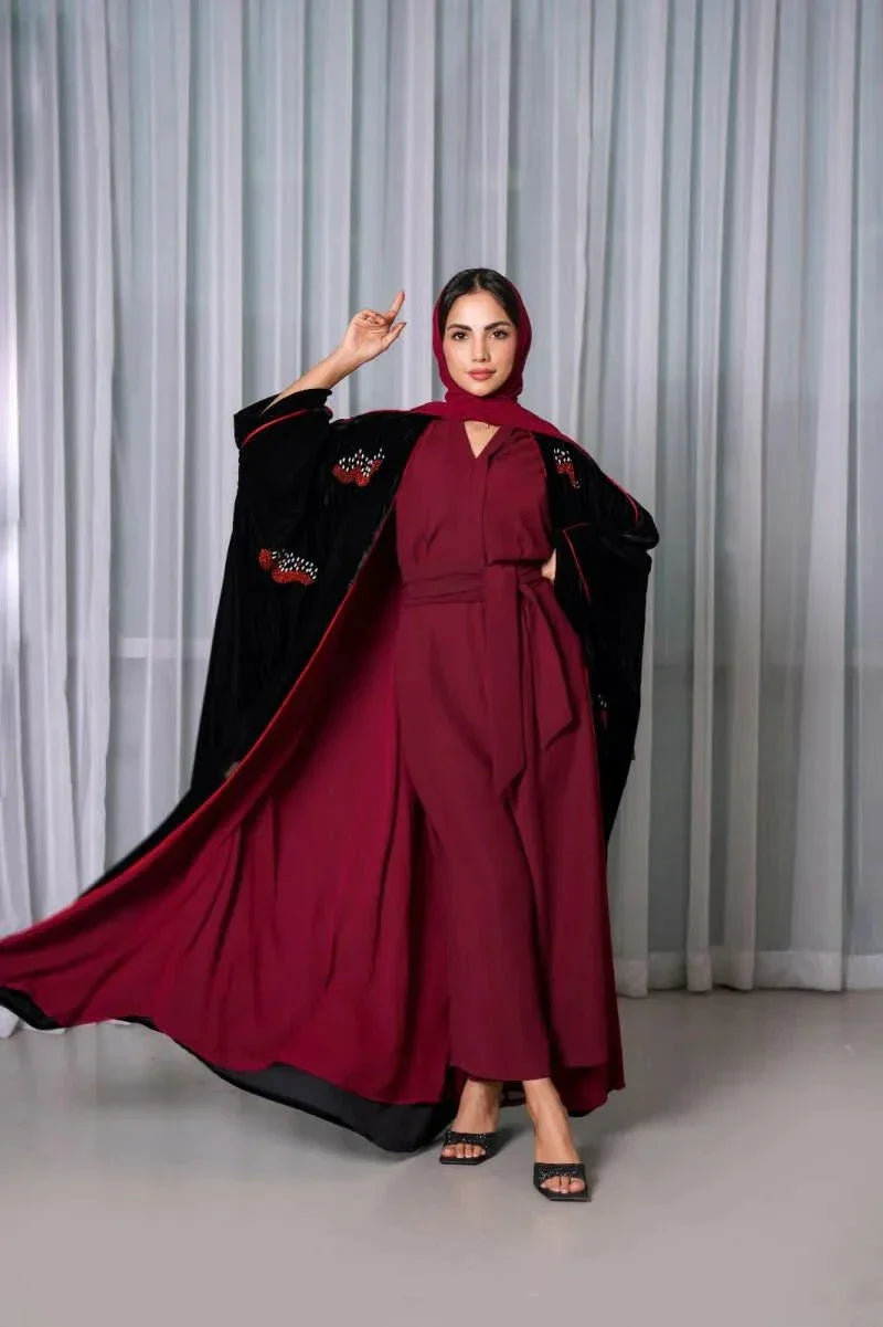 Luxurious black velvet bisht with red stone hand embroidery worn over a maroon outfit by a woman standing indoors.