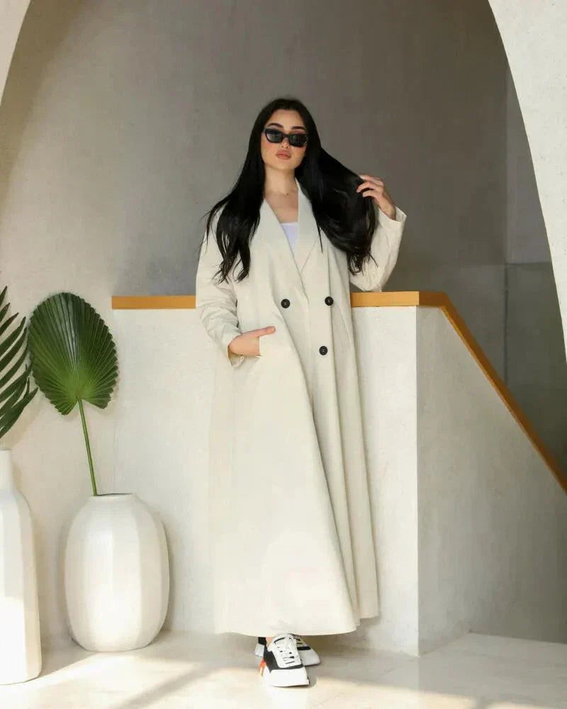 Cream blazer-style abaya with double-breasted black buttons and side pockets, tailored in structured crepe fabric for a modern classic look.