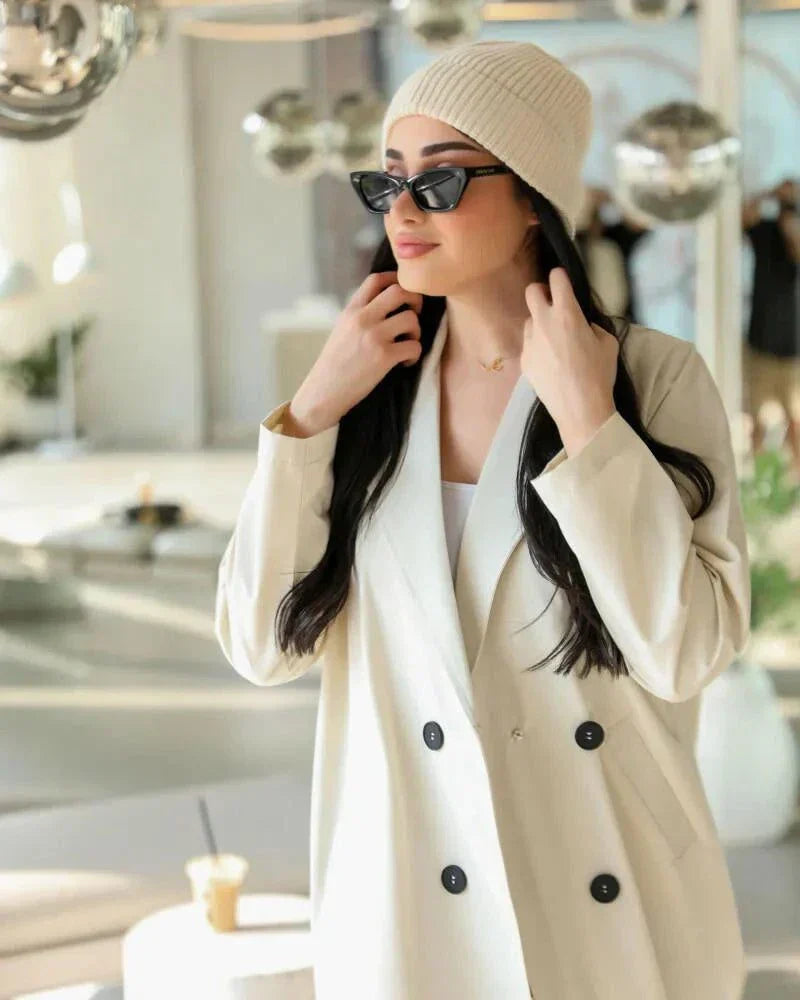 Cream blazer-style abaya with double-breasted black buttons and side pockets, tailored in structured crepe fabric for a modern classic look.