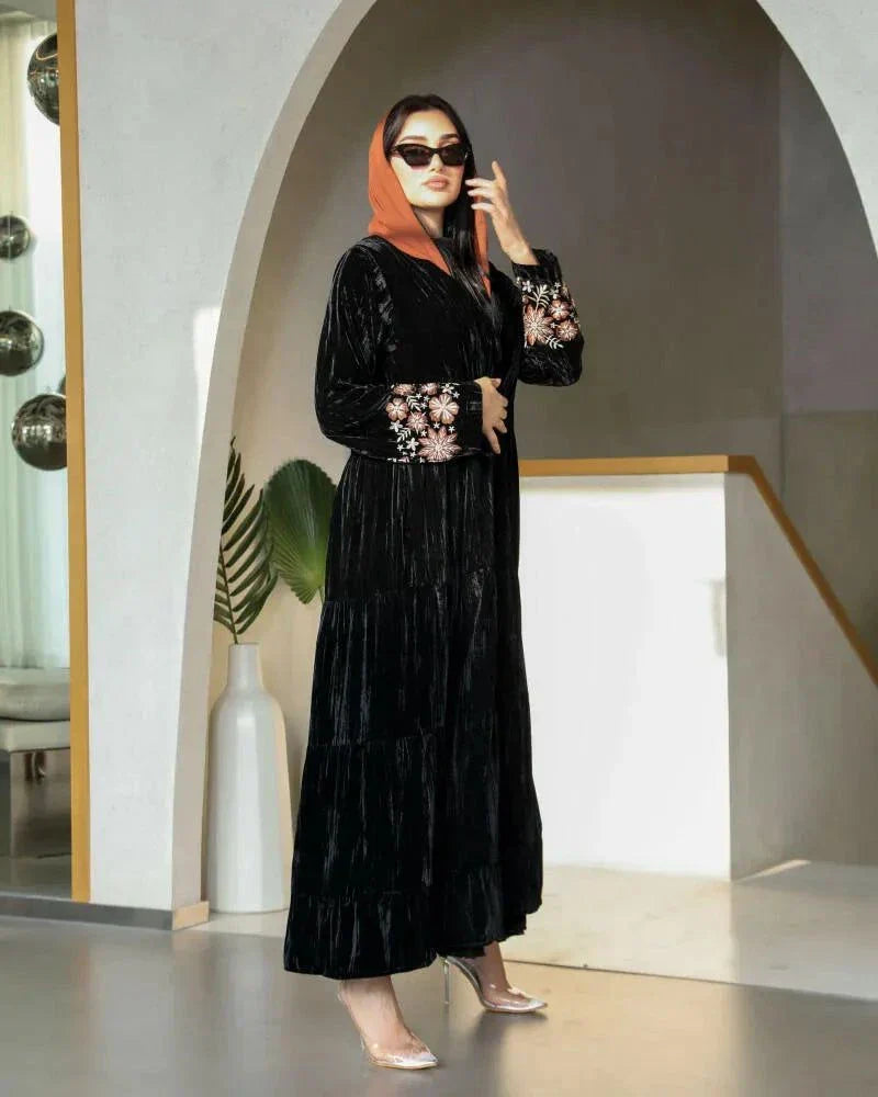 Elegant flowy black abaya made of wrinkled velvet with pink and peach floral embroidery on sleeves, styled for cooler seasons.