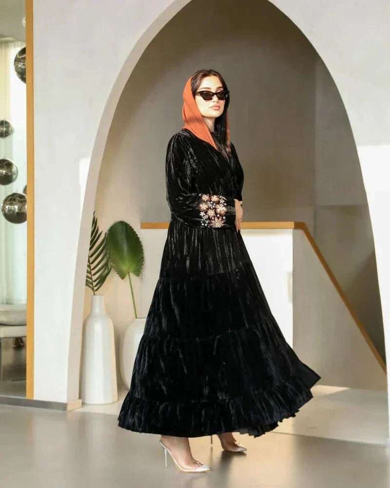 Elegant flowy black abaya made of wrinkled velvet with pink and peach floral embroidery on sleeves, styled for cooler seasons.