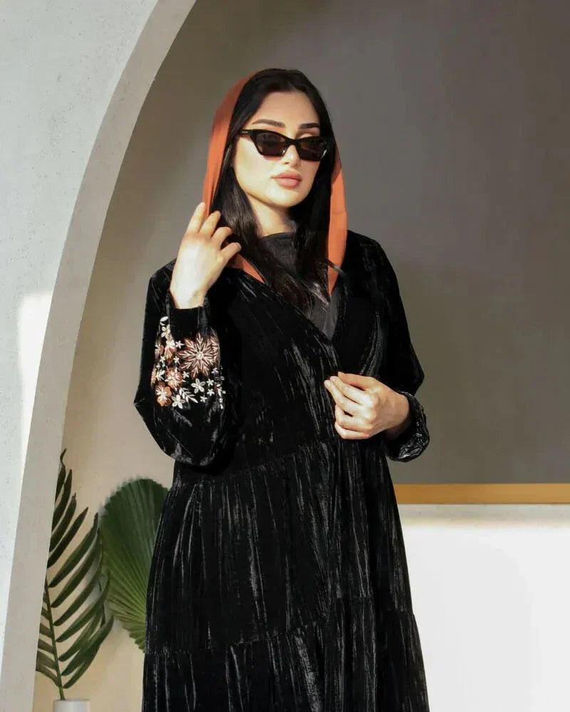 Elegant flowy black abaya made of wrinkled velvet with pink and peach floral embroidery on sleeves, styled for cooler seasons.