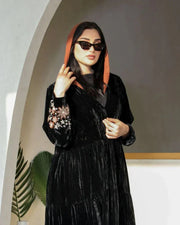 Elegant flowy black abaya made of wrinkled velvet with pink and peach floral embroidery on sleeves, styled for cooler seasons.