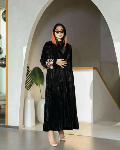 Elegant flowy black abaya made of wrinkled velvet with pink and peach floral embroidery on sleeves, styled for cooler seasons.