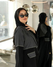 Woman wearing Ashden black abaya with gray washed-jean two-tone panel, contrast stitching, and flap pocket in modern urban style