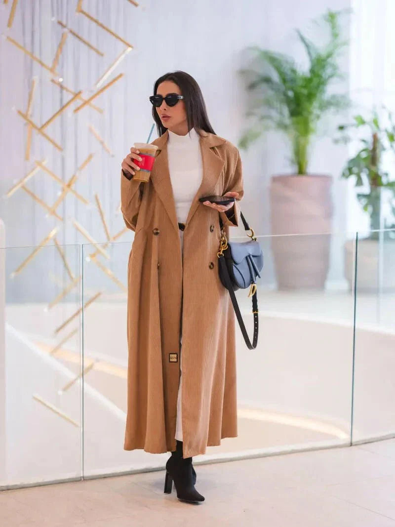 Woman wearing a caramel abaya with double-breasted buttons and soft shoulder seams, styled with black boots and sunglasses.