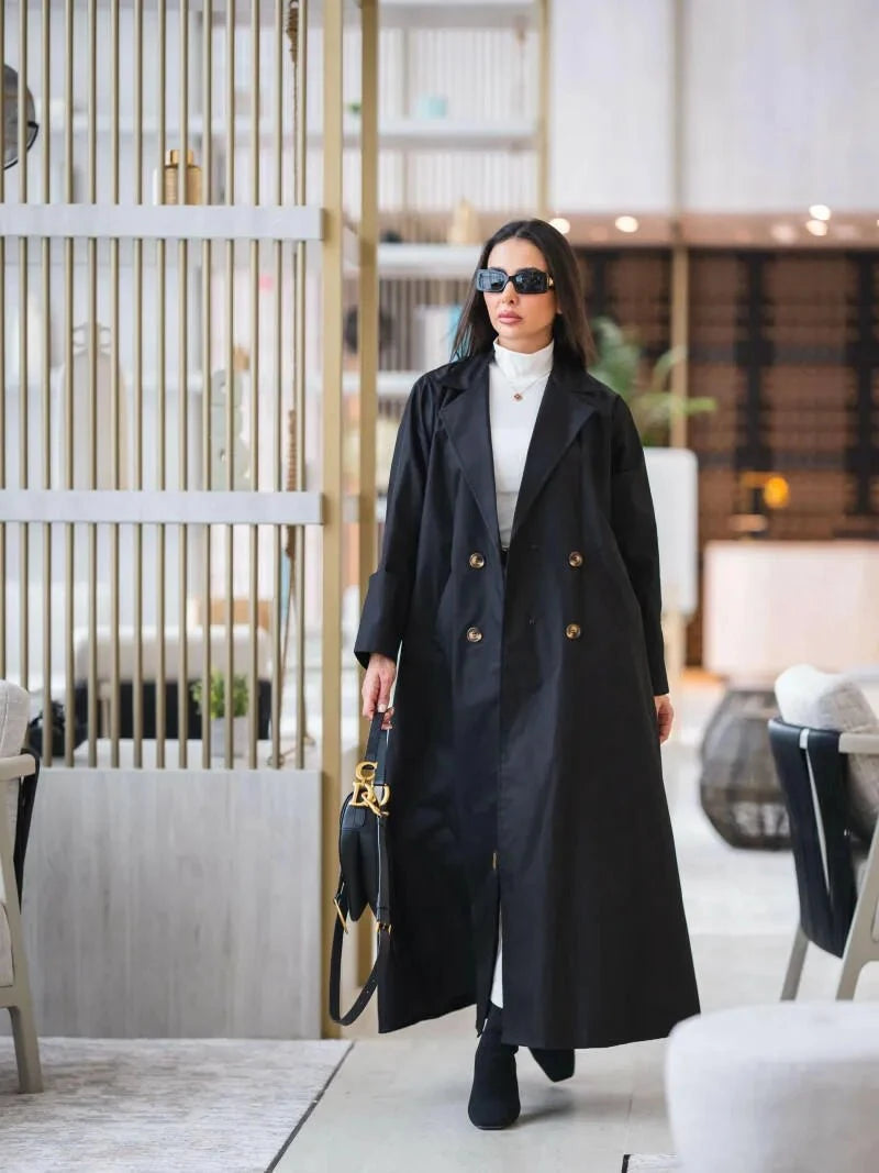 Woman wearing a structured black abaya trench coat with gold buttons and sharp lapels walking indoors