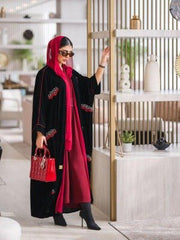 Elegant black velvet abaya with burgundy and white embroidery, styled with a red headscarf and matching red handbag.