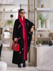 Elegant black velvet abaya with burgundy and white embroidery, styled with a red headscarf and matching red handbag.