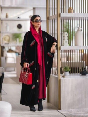 Elegant black velvet abaya with burgundy and white embroidery, styled with a red headscarf and matching red handbag.