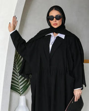 Woman wearing a sleek black abaya with blazer-inspired design, lapel collar, and gathered waist.