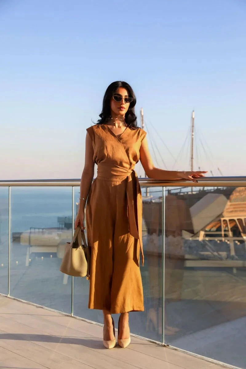 Woman wearing camel linen sleeveless jumpsuit with wrap V-neck and waist tie by the seaside