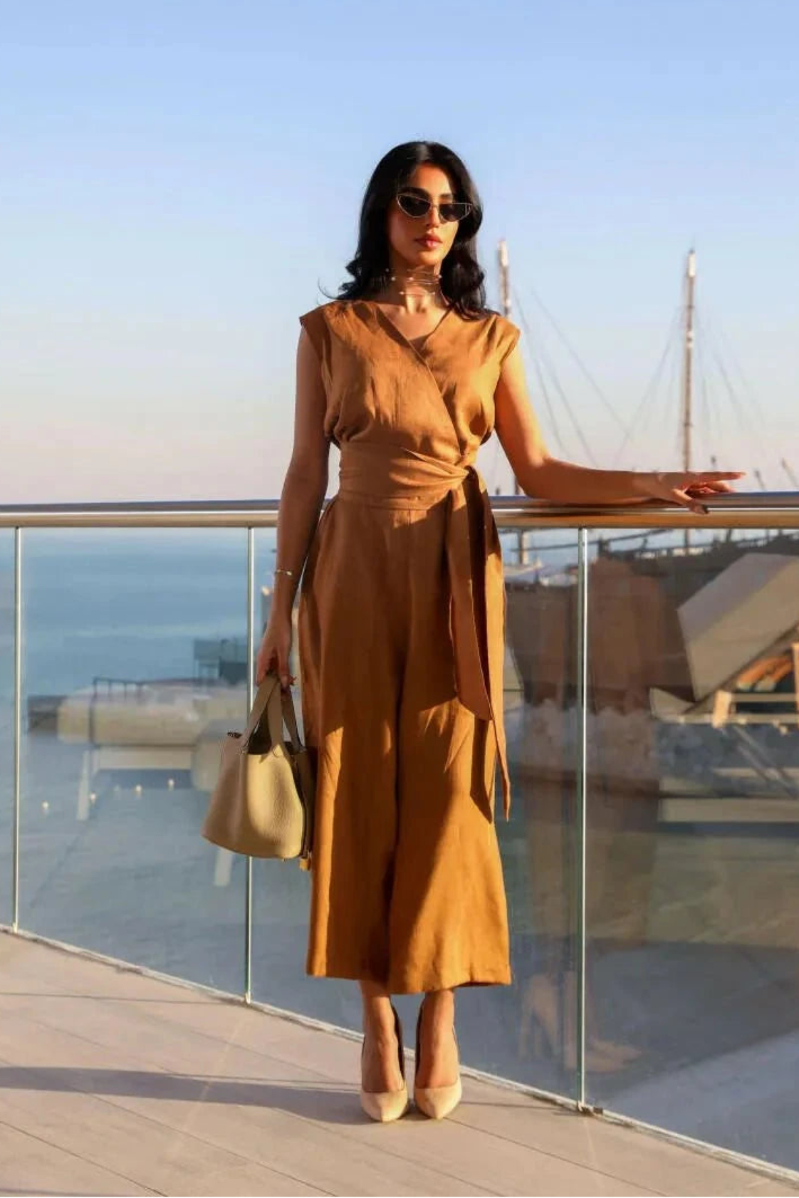 Woman wearing camel linen sleeveless jumpsuit with wrap V-neck and waist tie by the seaside