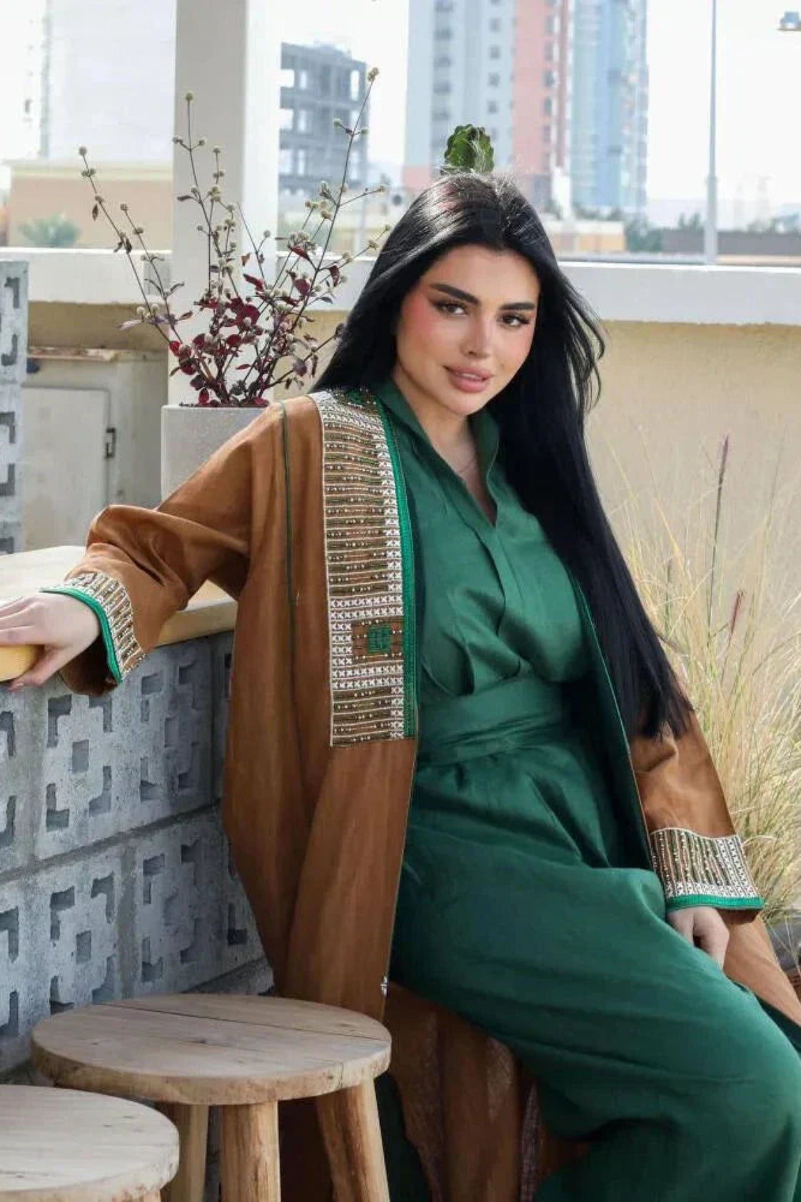 Woman wearing camel-brown linen abaya with green and gold embroidery and piping, styled over a green outfit, sitting outdoors - Honeywood