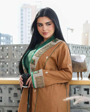 Woman wearing camel-brown linen abaya with green and gold embroidery and piping, styled over a green outfit, sitting outdoors - Honeywood