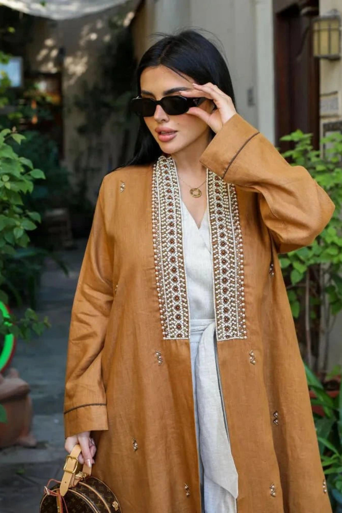 woman wearing caramel-brown linen abaya with pearl-embroidered front panels and subtle cuff detailing outdoors