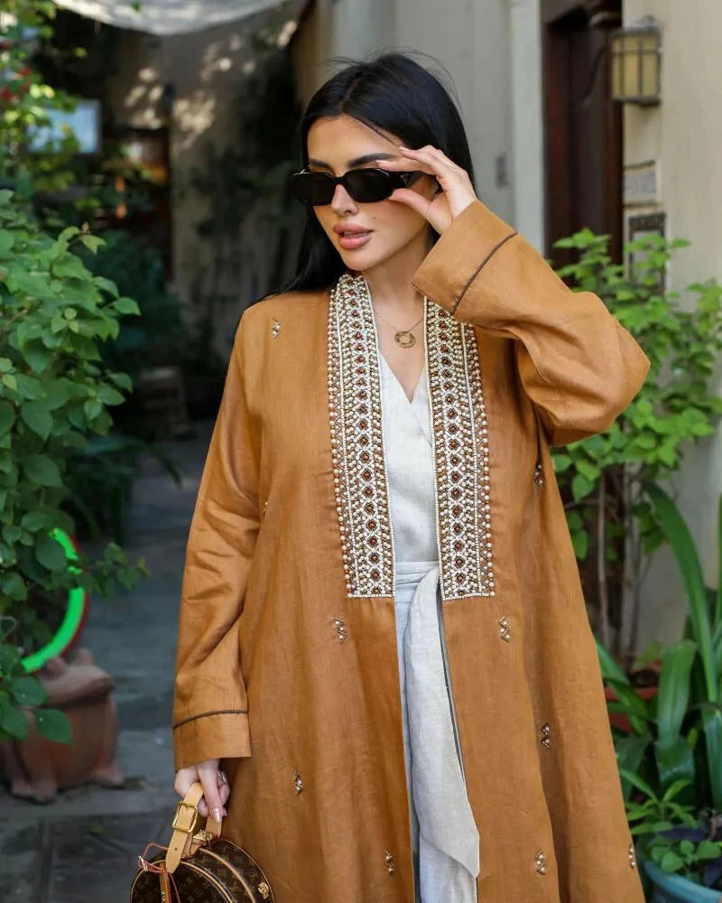 woman wearing caramel-brown linen abaya with pearl-embroidered front panels and subtle cuff detailing outdoors