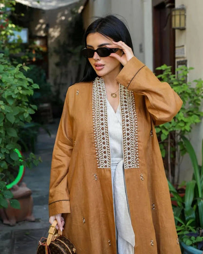 woman wearing caramel-brown linen abaya with pearl-embroidered front panels and subtle cuff detailing outdoors
