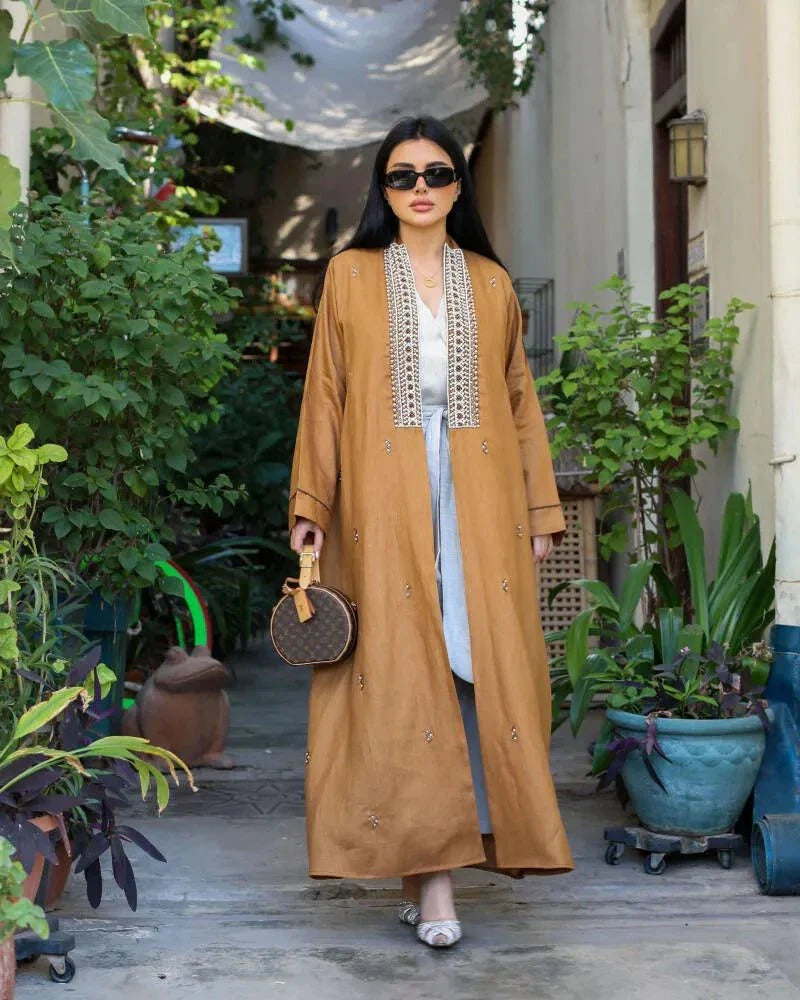 Woman wearing caramel-brown linen abaya with pearl embroidery and subtle embellishments walking outdoors