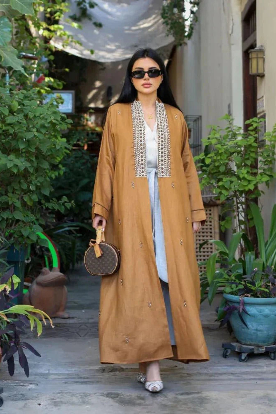 Woman wearing caramel-brown linen abaya with pearl embroidery and subtle embellishments walking outdoors