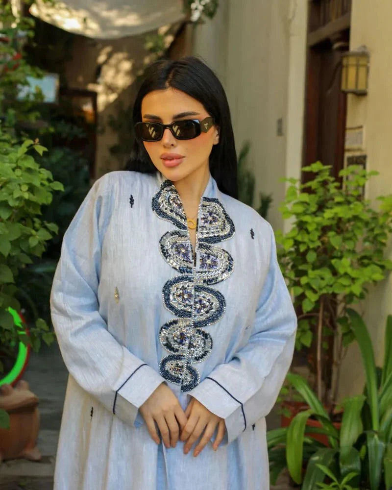Woman wearing a soft sky-blue abaya with embroidered front panels and a flowy linen design outdoors
