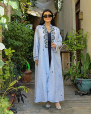 woman wearing soft sky-blue abaya with tonal embroidery in outdoor garden setting