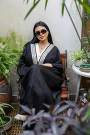 Woman wearing black linen bisht with gold embroidery over white outfit standing outdoors