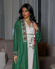 woman wearing vibrant green linen abaya with traditional red, white, and beige embroidery on front panels, cuffs, and collar, styled over light beige outfit