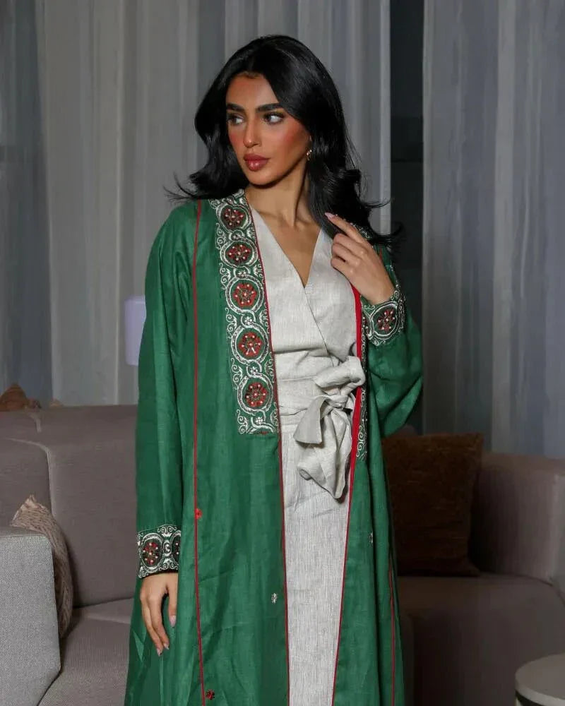 woman wearing vibrant green linen abaya with traditional red, white, and beige embroidery on front panels, cuffs, and collar, styled over light beige outfit