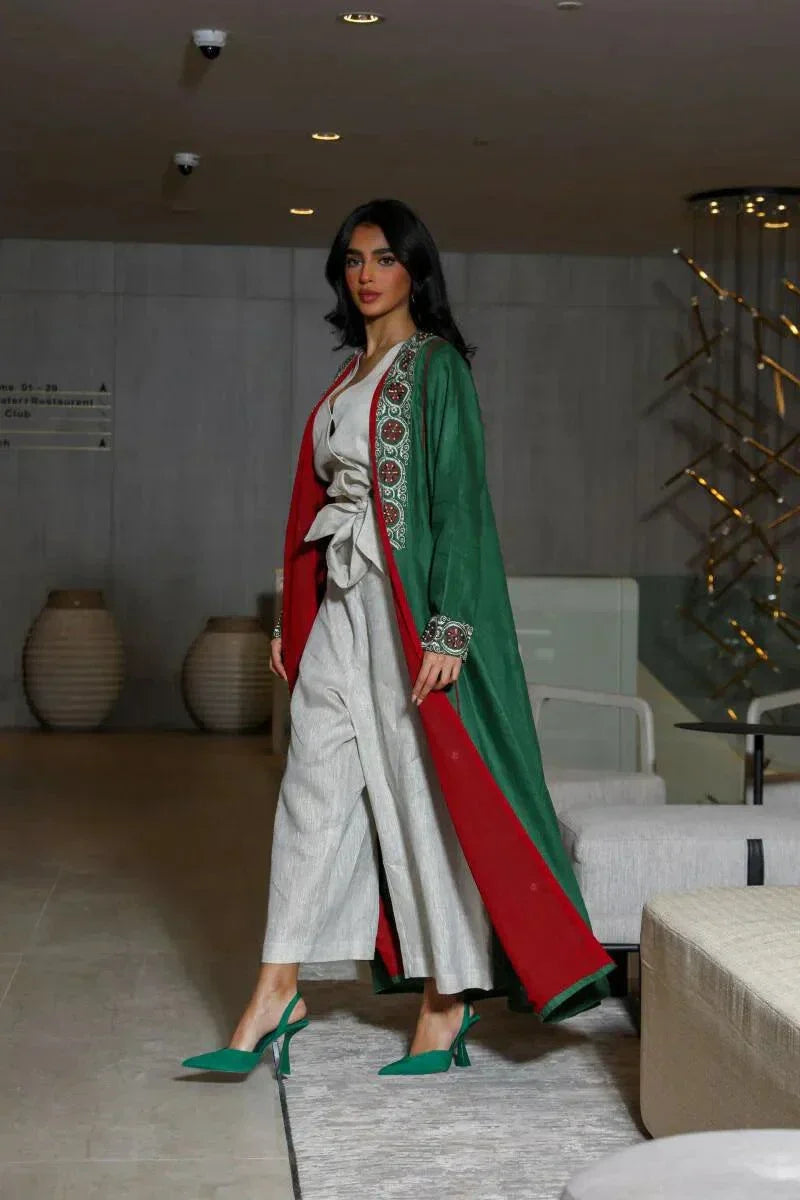 woman wearing vibrant green linen abaya with traditional red, white, and beige embroidery on front panels, cuffs, and collar, styled over light beige outfit