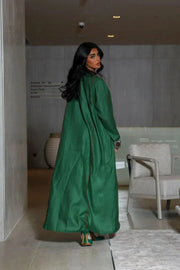 woman wearing vibrant green linen abaya with traditional red, white, and beige embroidery on front panels, cuffs, and collar, styled over light beige outfit