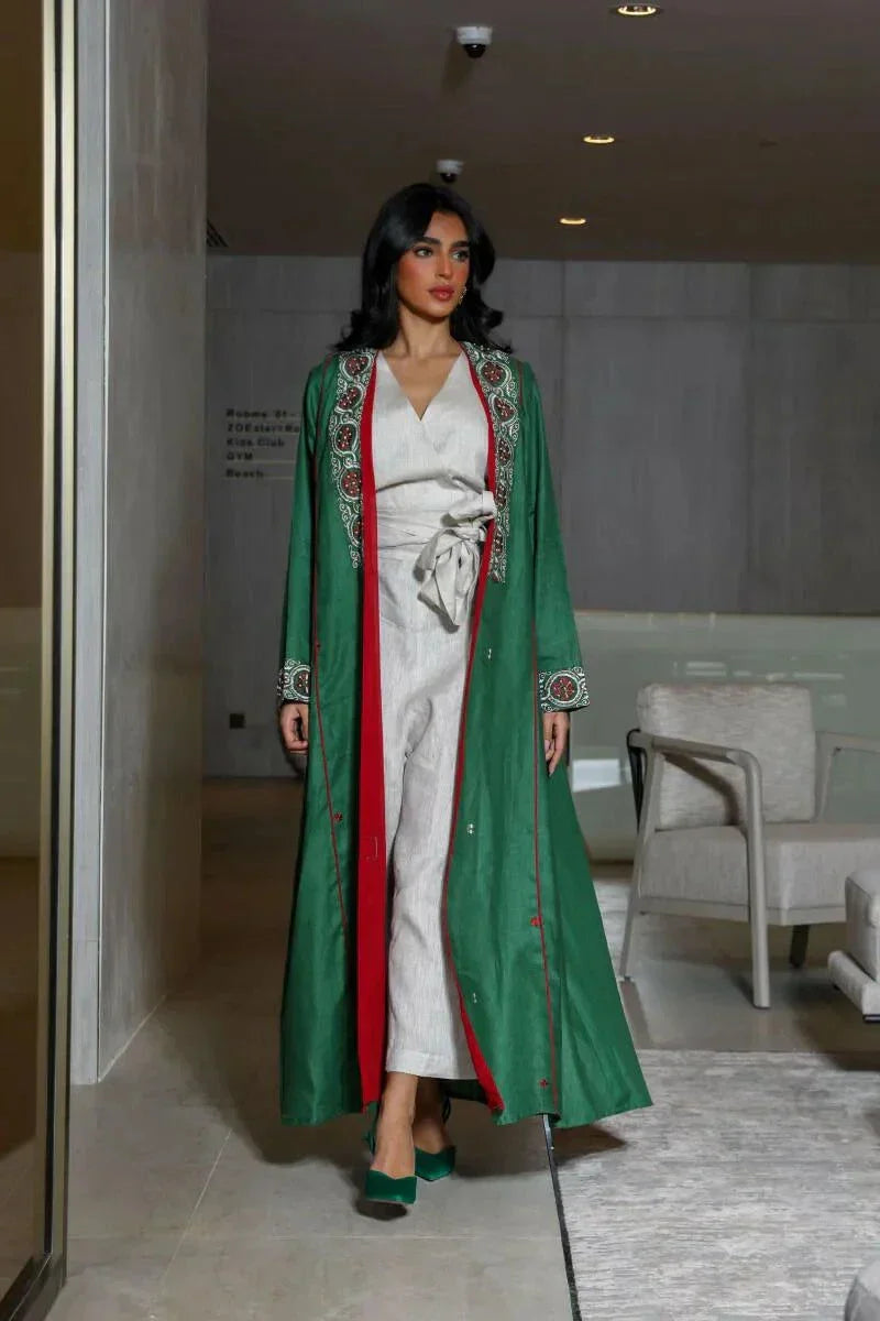 woman wearing vibrant green linen abaya with traditional red, white, and beige embroidery on front panels, cuffs, and collar, styled over light beige outfit